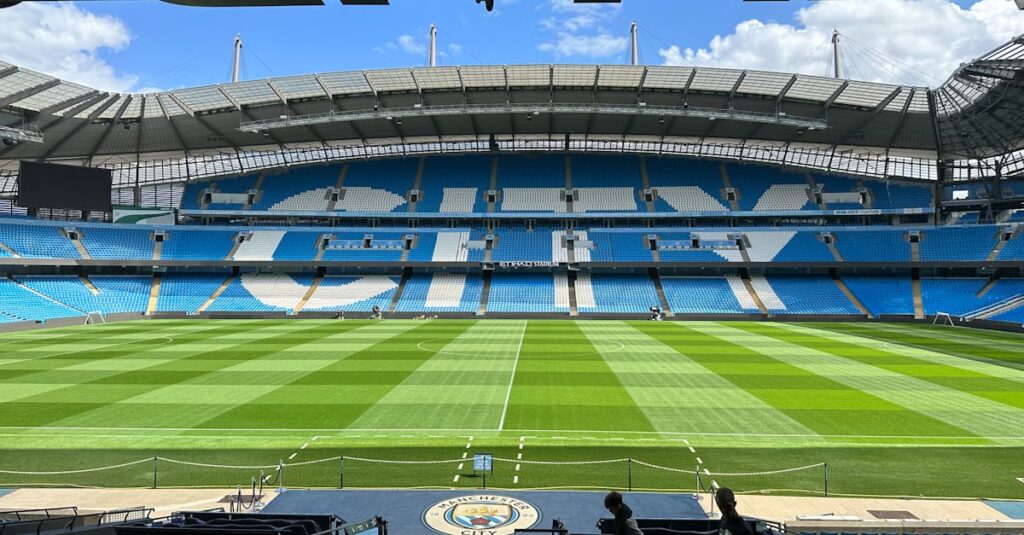 Panoramic view of Etihad Stadium, showcasing the empty football pitch and stands under a clear blue sky.